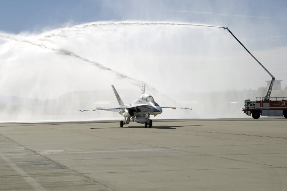 An F-18 aircraft taxies beneath the spray from fire trucks Canvas Art - Stocktrek Images (34 x 23)