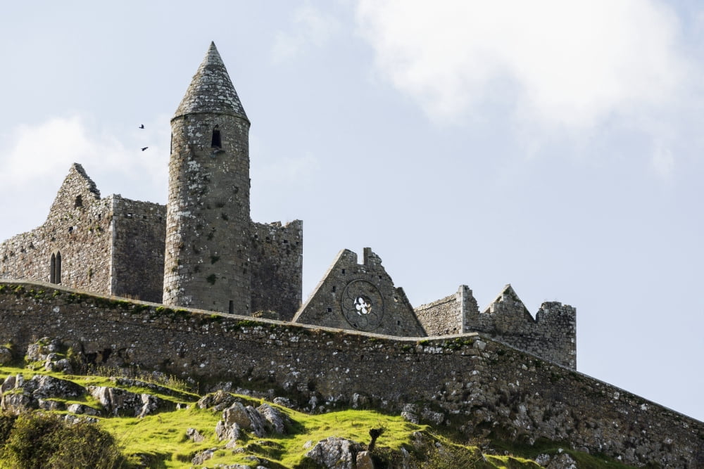Ancient stone ruin with stone wall turret and church on rocky grassy hillside with blue sky and clouds Cashel County Tipperary Ireland Canvas Art - Michael Interisano Design Pics (38 x 24)