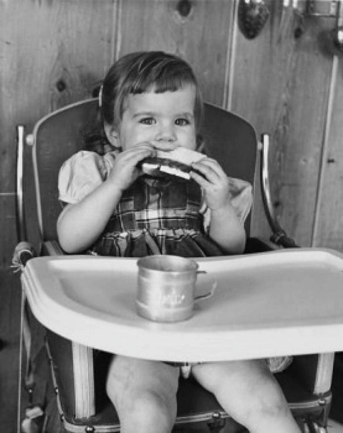 Baby girl sitting in a high chair and eating a slice of bread Canvas Art - (18 x 24)