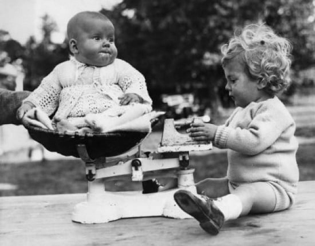 Baby girl sitting on scales bowl and older brother weighting her Canvas Art - (24 x 36)
