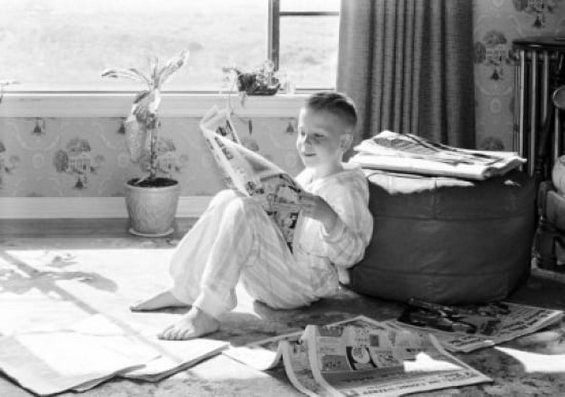 Boy leaning against hassock reading newspaper Canvas Art - (24 x 36)