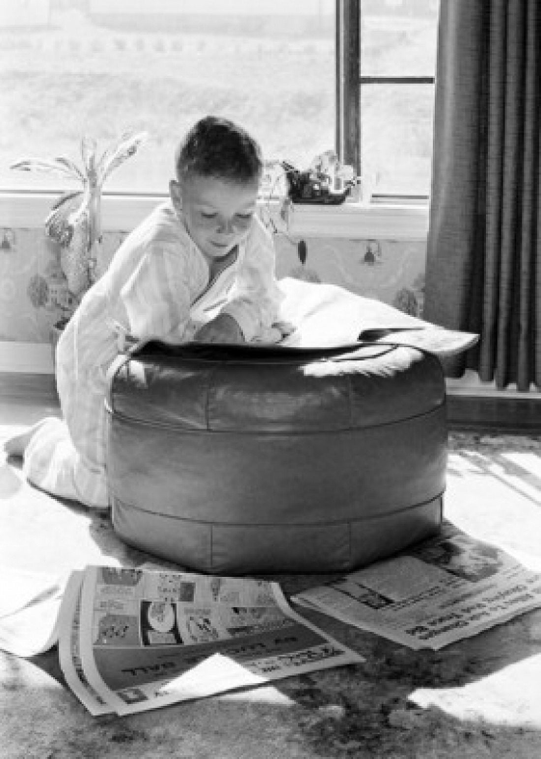 Boy leaning on hassock reading newspaper Canvas Art - (24 x 36)