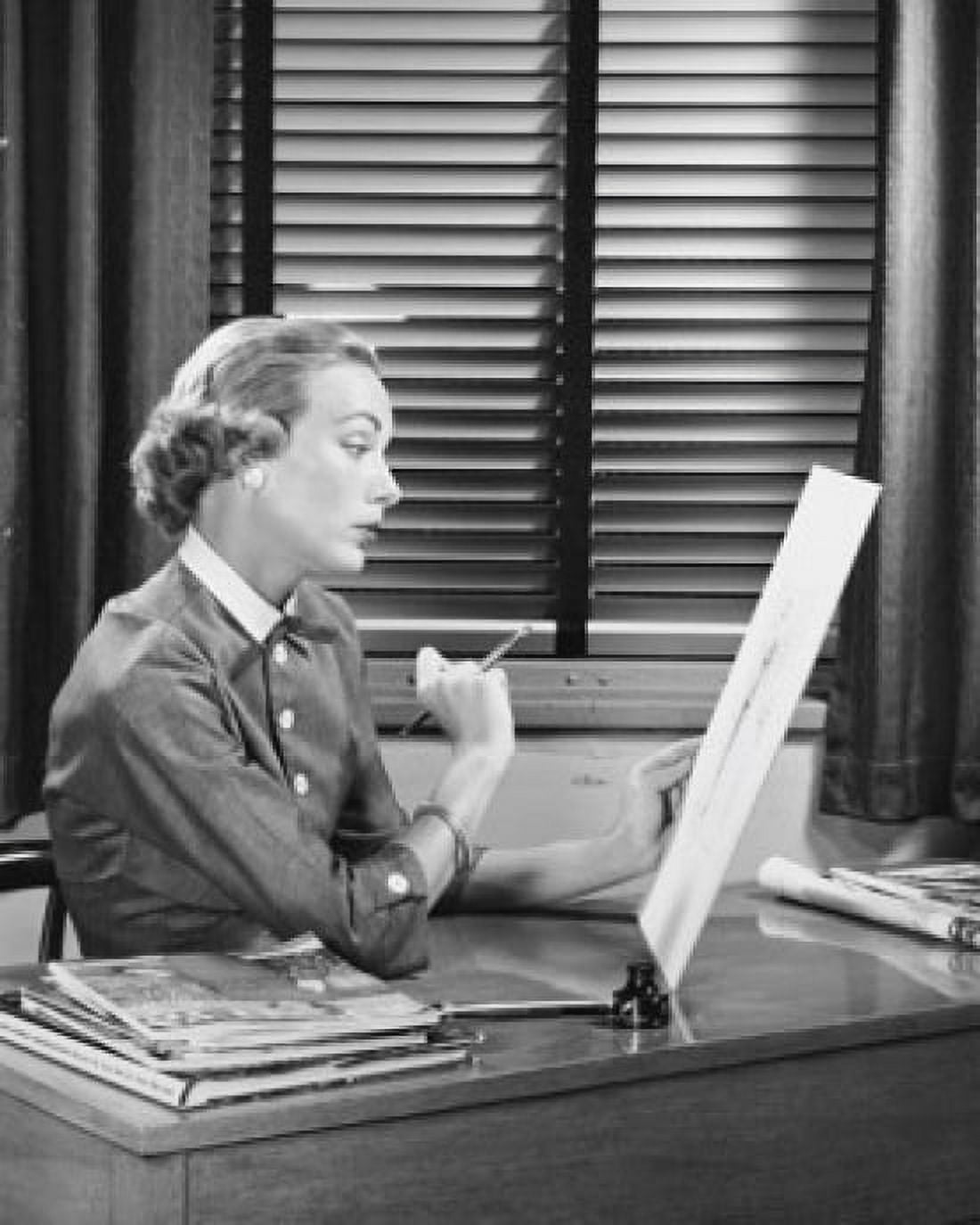 Businesswoman sitting at a desk and looking at a sketch pad in an office Canvas Art - (24 x 36)