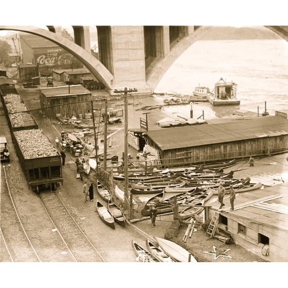 Canoes abound as flood waters lap the shore under concrete bridge and beside railroad hopper cars. Poster Print (18 x