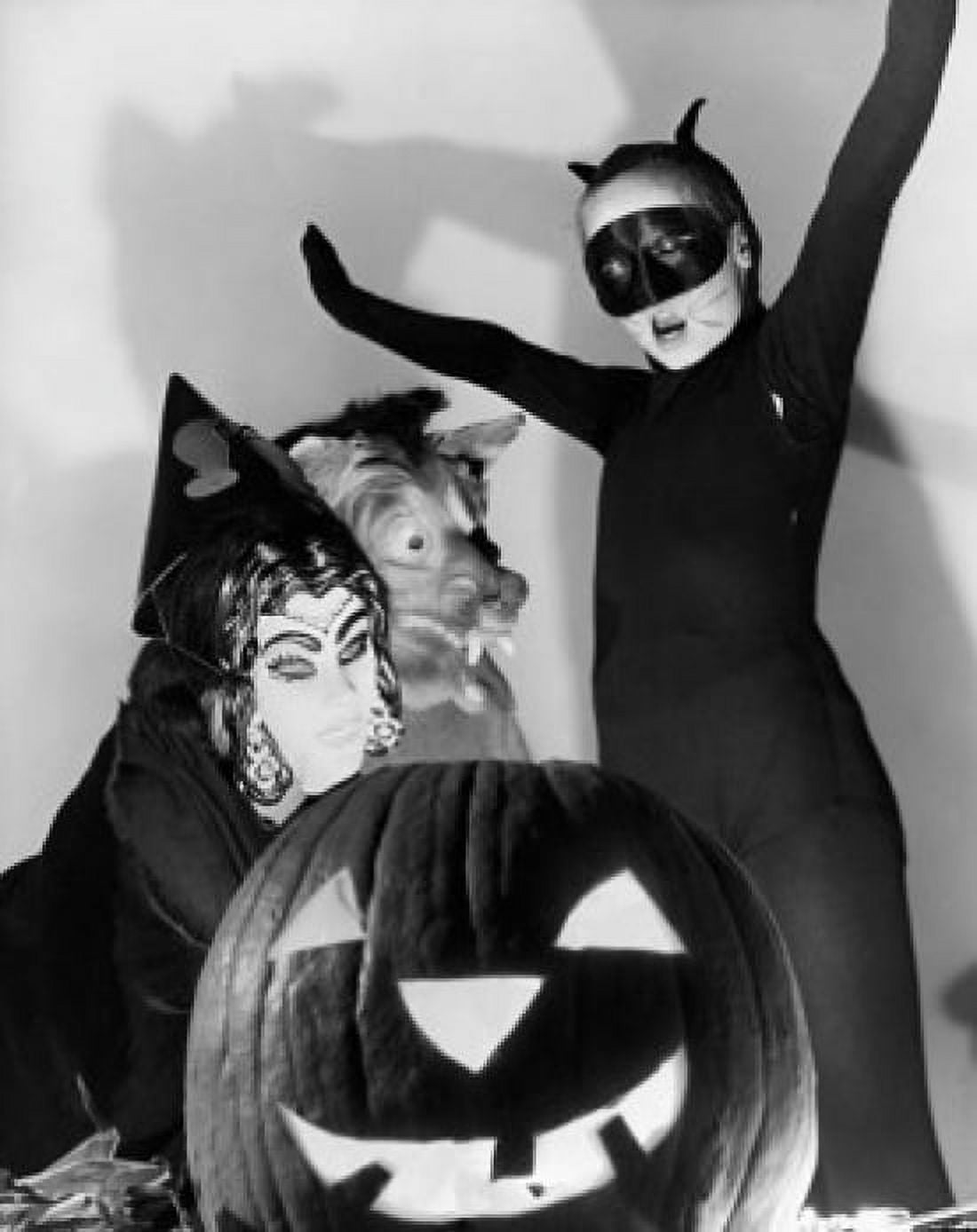 Close-up of an illuminated jack o lantern with three people wearing Halloween costumes behind it Canvas Art - (24 x 36)