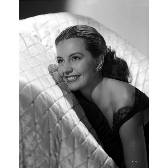 Cyd Charisse smiling in a White Couch wearing Black Sleeveless Dress and an Earrings Photo Print (8 x 10)
