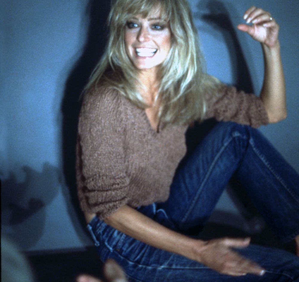 Farrah Fawcett wearing a brown sweater and blue jeans, sitting with ...