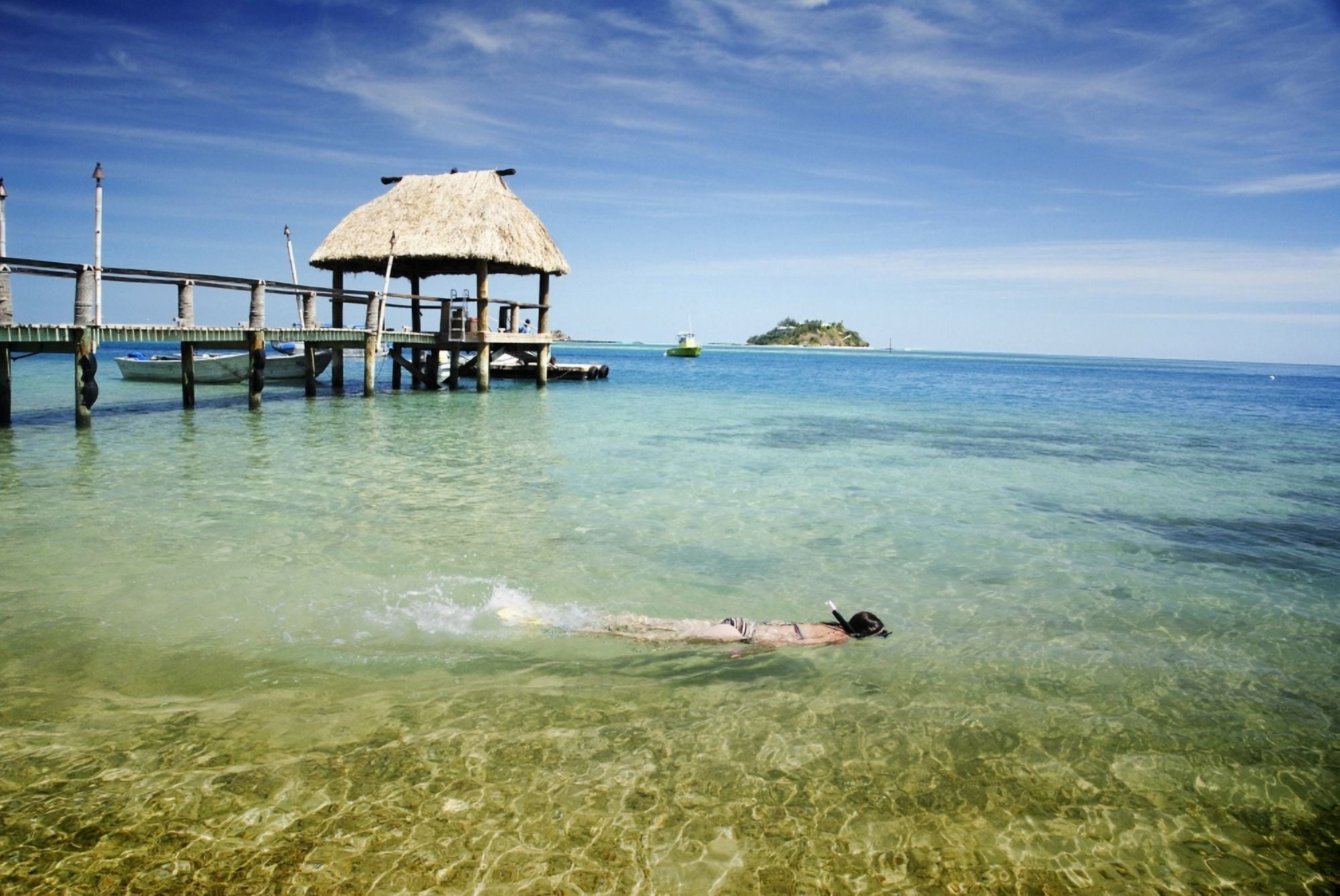 Fiji Mamanuca Islands Wadigi Island in distance Malolo Island Snorkeler in clear ocean besides pier with fijian style thatched bure roof Canvas Art - Himani Smeaton Design Pics (17 x 11)
