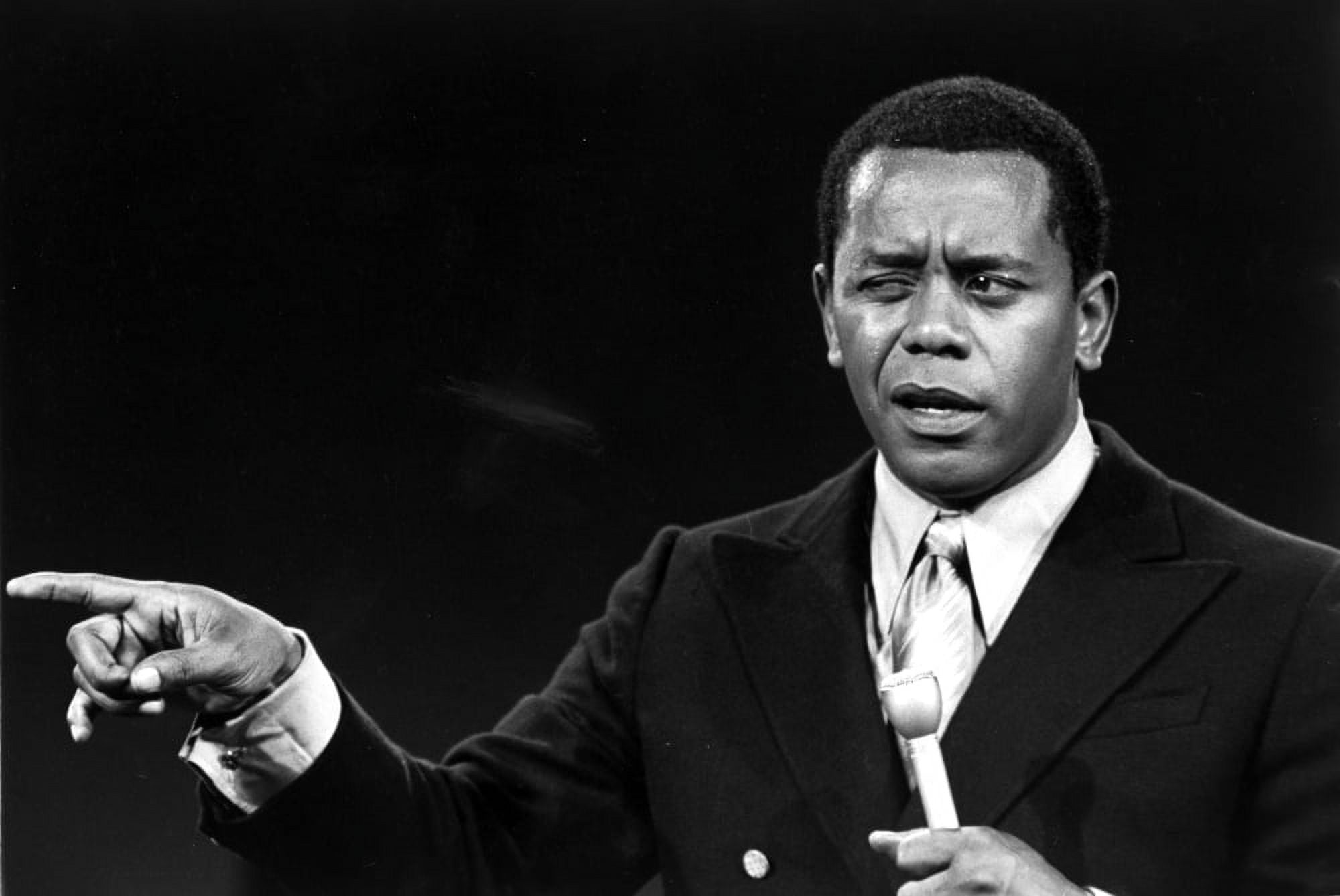 Flip Wilson on stage with a microphone pointing Photo Print (24 x 30)