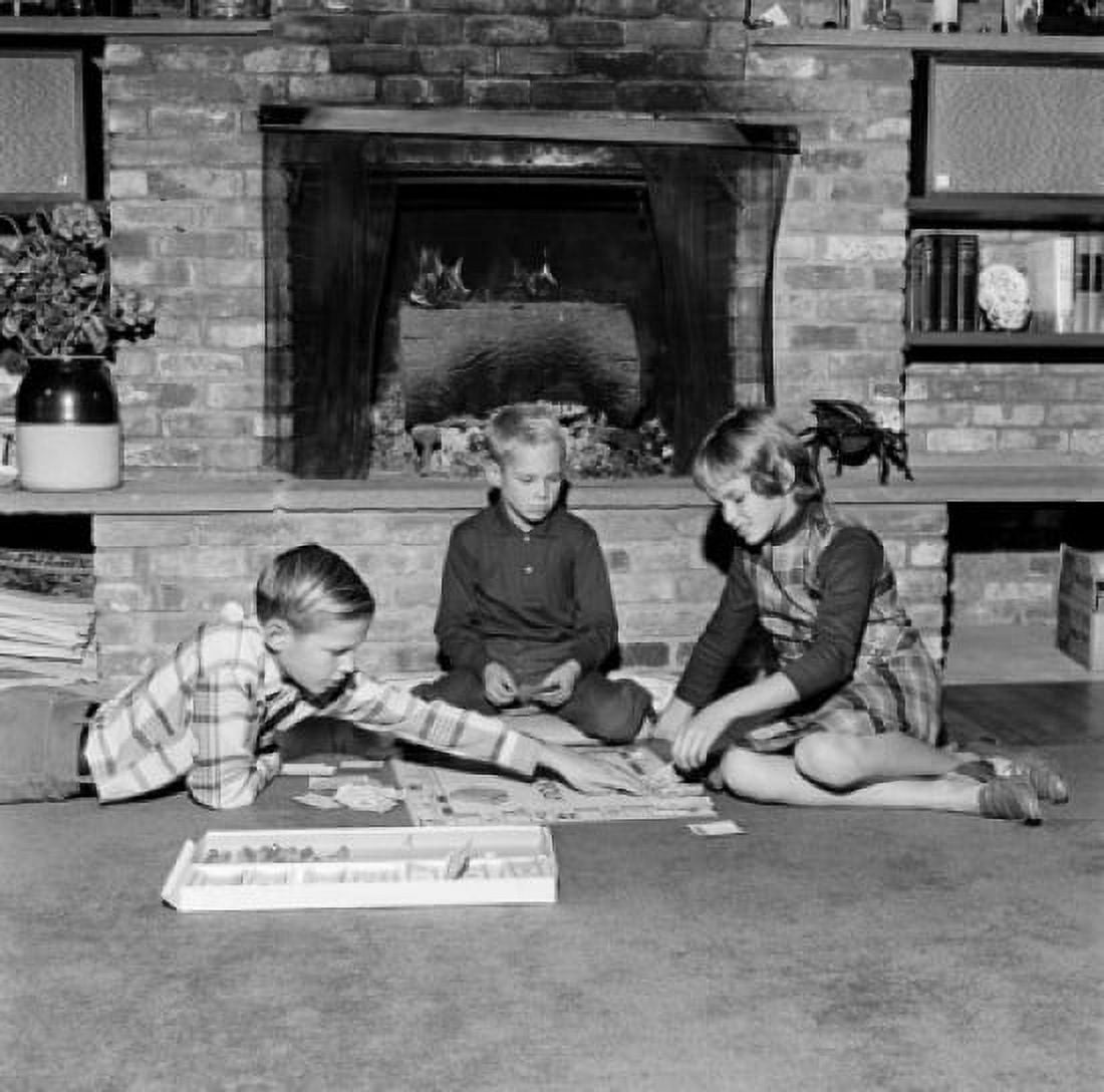 Girl and two boys playing monopoly in front of fireplace Canvas Art -  (24 x 36)