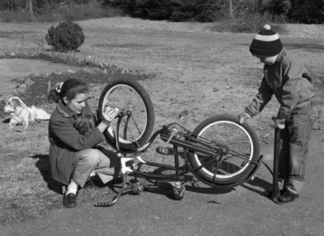 Girl oiling front wheel as young boy pumps air into the rear tire of a bike Canvas Art - (24 x 36)
