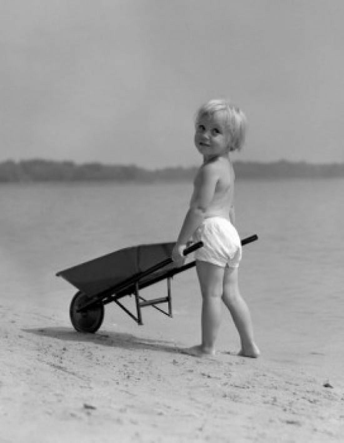 Girl pushing toy wheelbarrow on beach Canvas Art - (18 x 24)
