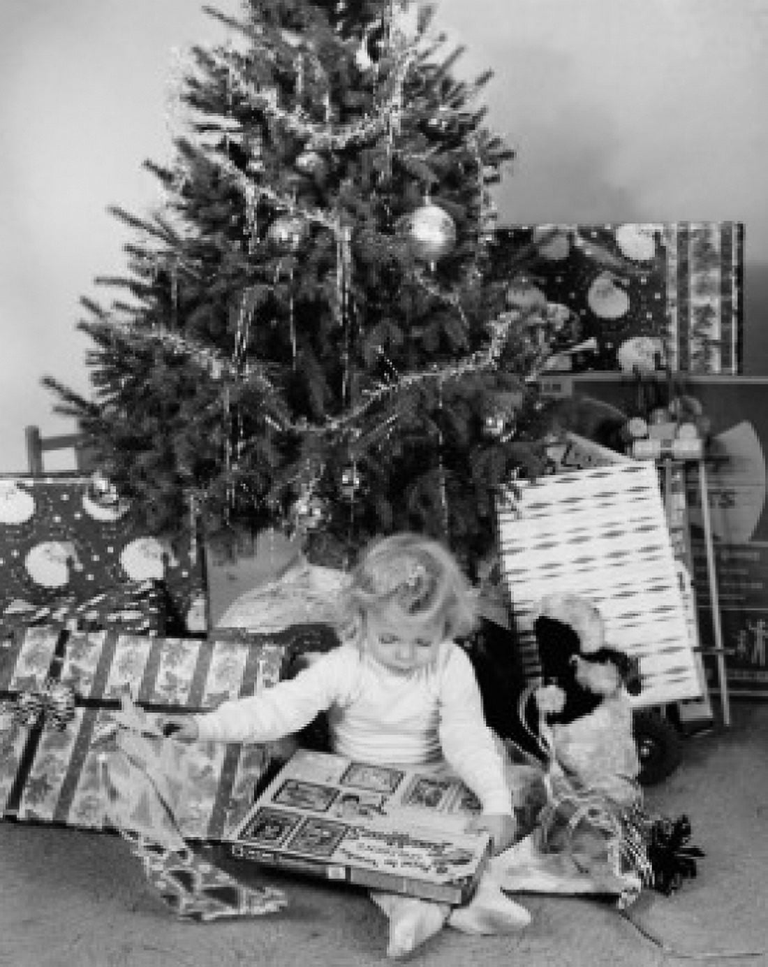 Girl sitting in front of a Christmas tree and opening a Christmas present Canvas Art - (18 x 24)