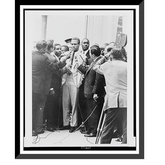 Historic Framed Print, [Malcolm X, full-length portrait, standing, facing slightly left, being interviewed by reporters].World Telegram & Sun photo by Herman Hiller., 17-7/8" x 21-7/8"