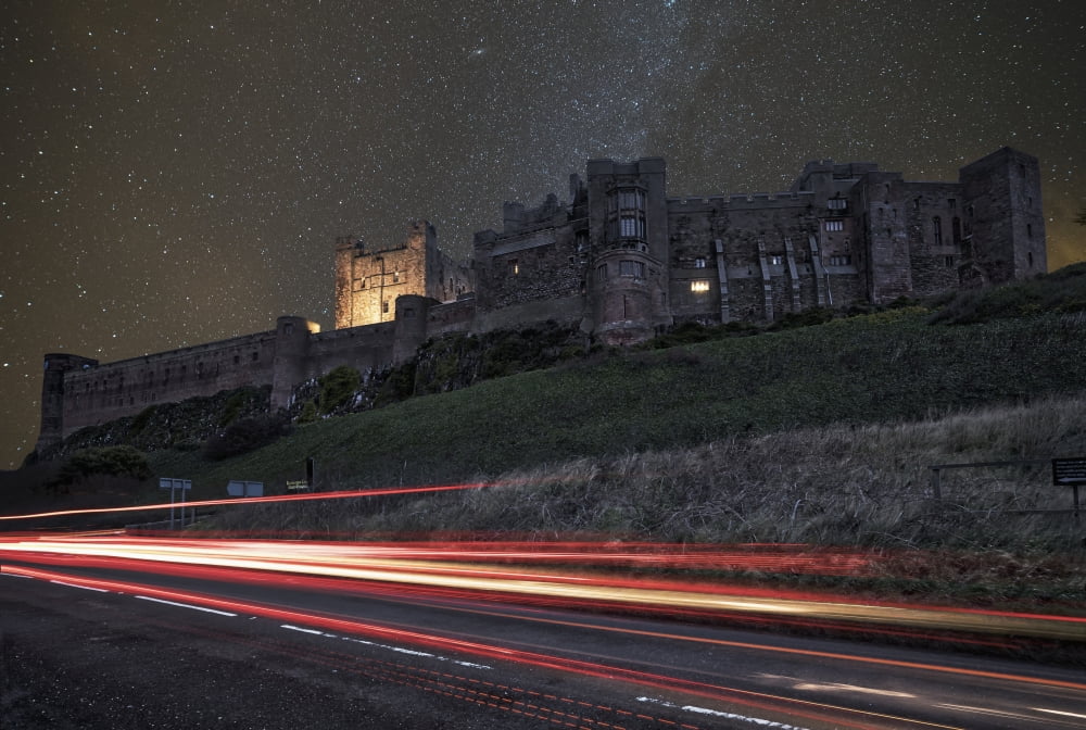 Light trails on a road and a star filled sky over Bamburgh Castle at nighttime Bamburgh Northumberland England Canvas Art - John Short Design Pics (19 x 12)