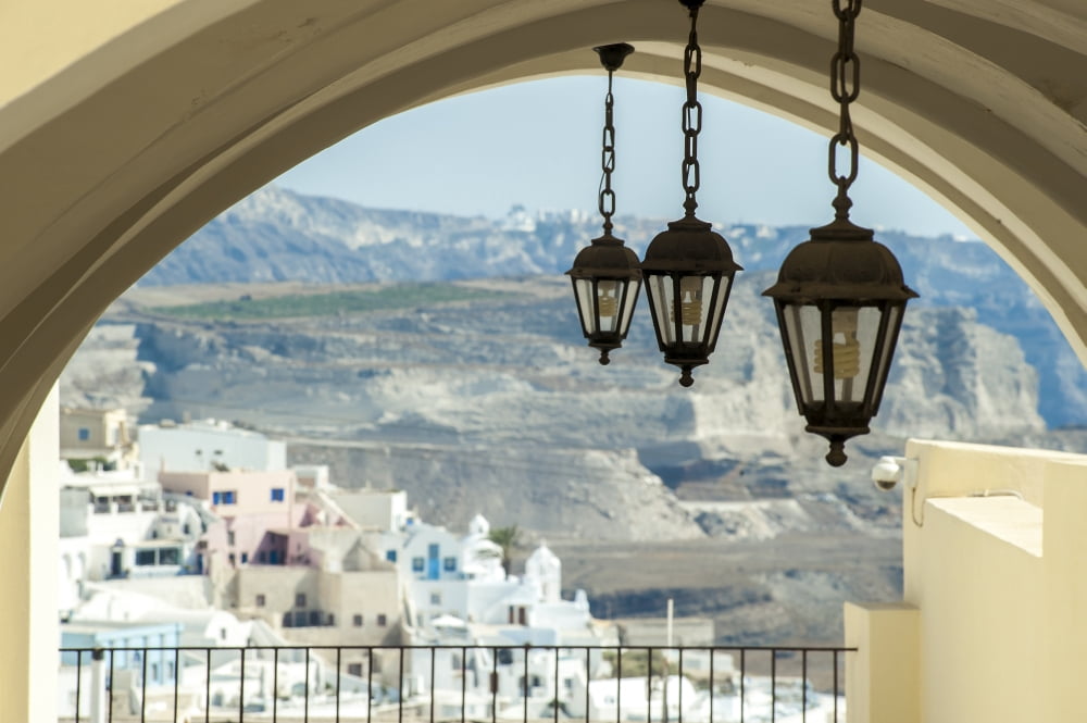 Lights hang from an arched ceiling with a view of a church whitewashed buildings and landscape Fira Santorini Greece Canvas Art - Dosfotos Design Pics (19 x 12)