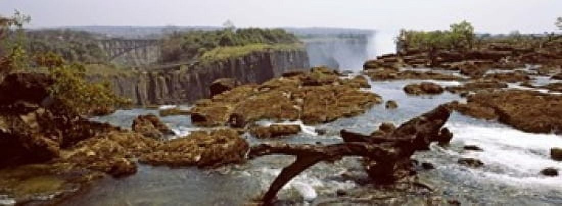 Log on the rocks at the top of the Victoria Falls with Victoria Falls Bridge in the background Zimbabwe Canvas Art - Panoramic Images (18 x 7)