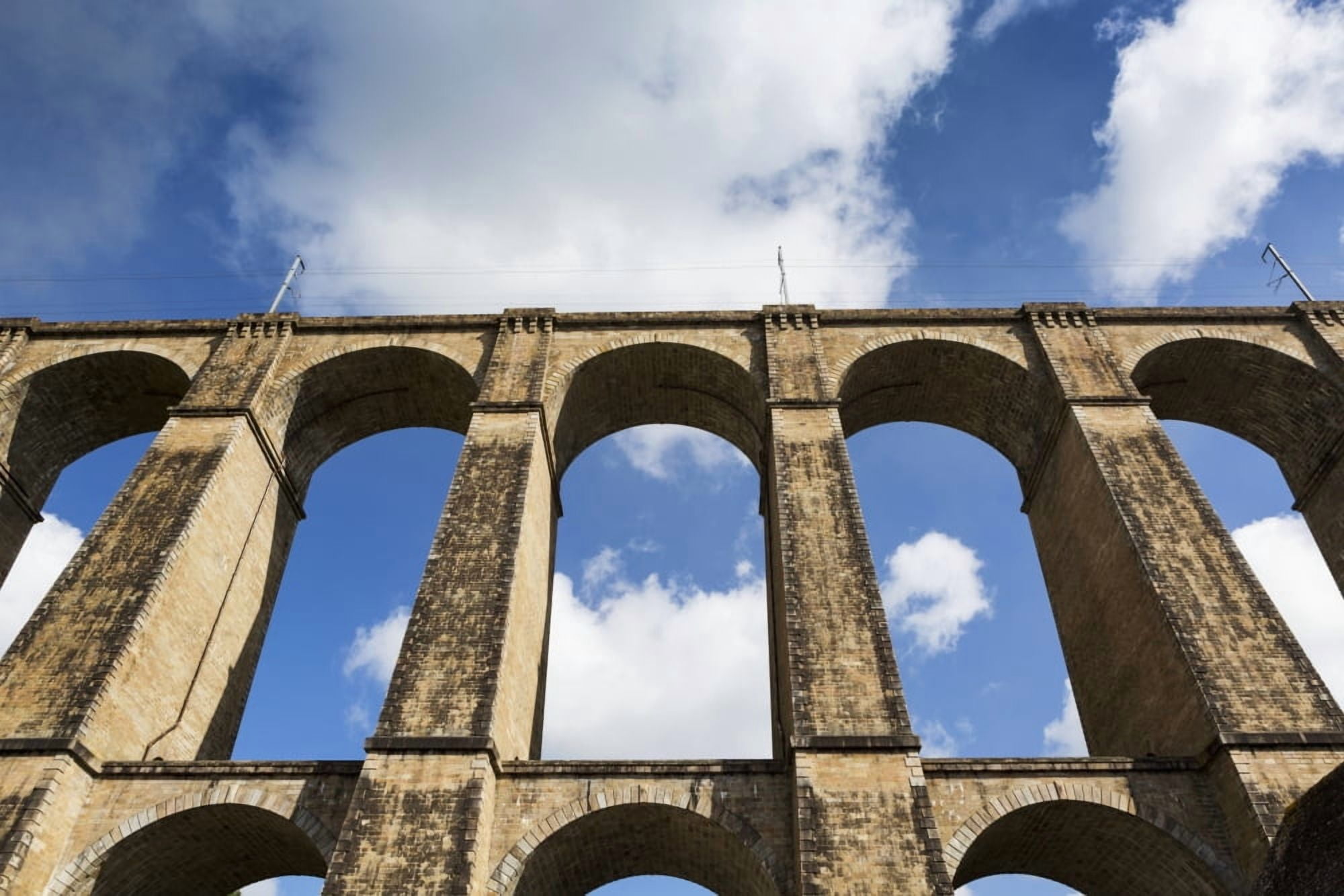 Low angle of a stone arched viaduct with blue sky and clouds Morlaix Brittany France Canvas Art - Michael Interisano Design Pics (19 x 12)
