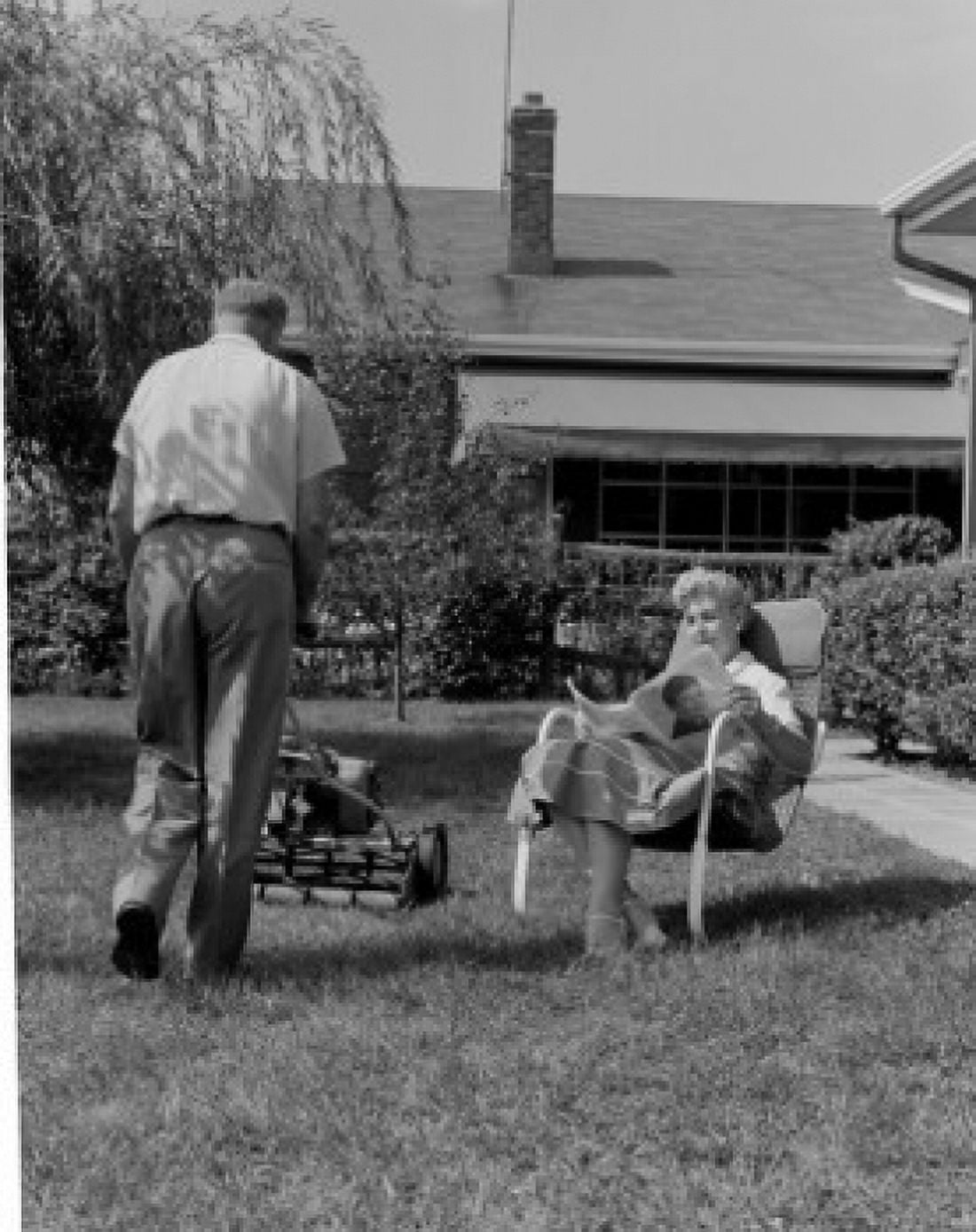 Man mowing lawn and woman reading newspaper in garden Canvas Art - (18 x 24)