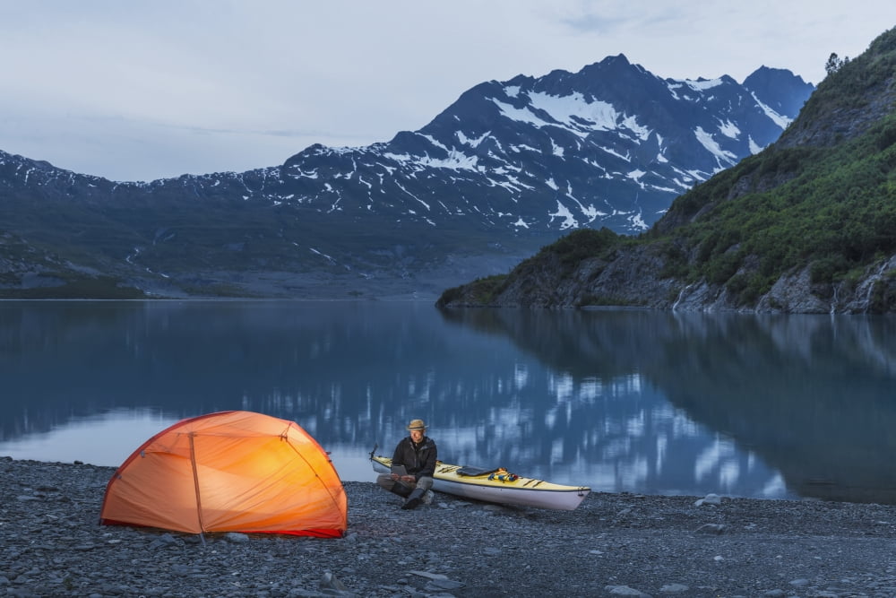 Man reading on a electronic tablet while camping with a tent and kayak at Shoup Bay State Marine Park Prince William sound Valdez Southcentral Alaska Canvas Art - Kevin Smith Design Pics (19 x 12)
