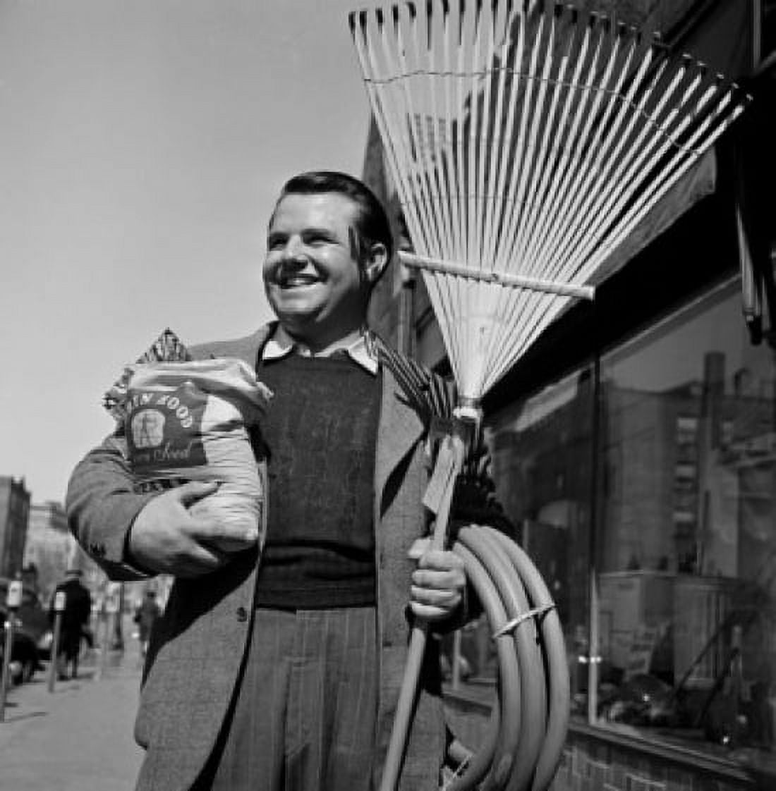 Man standing in street holding rake hose and seed bag Canvas Art - (24 x 36)