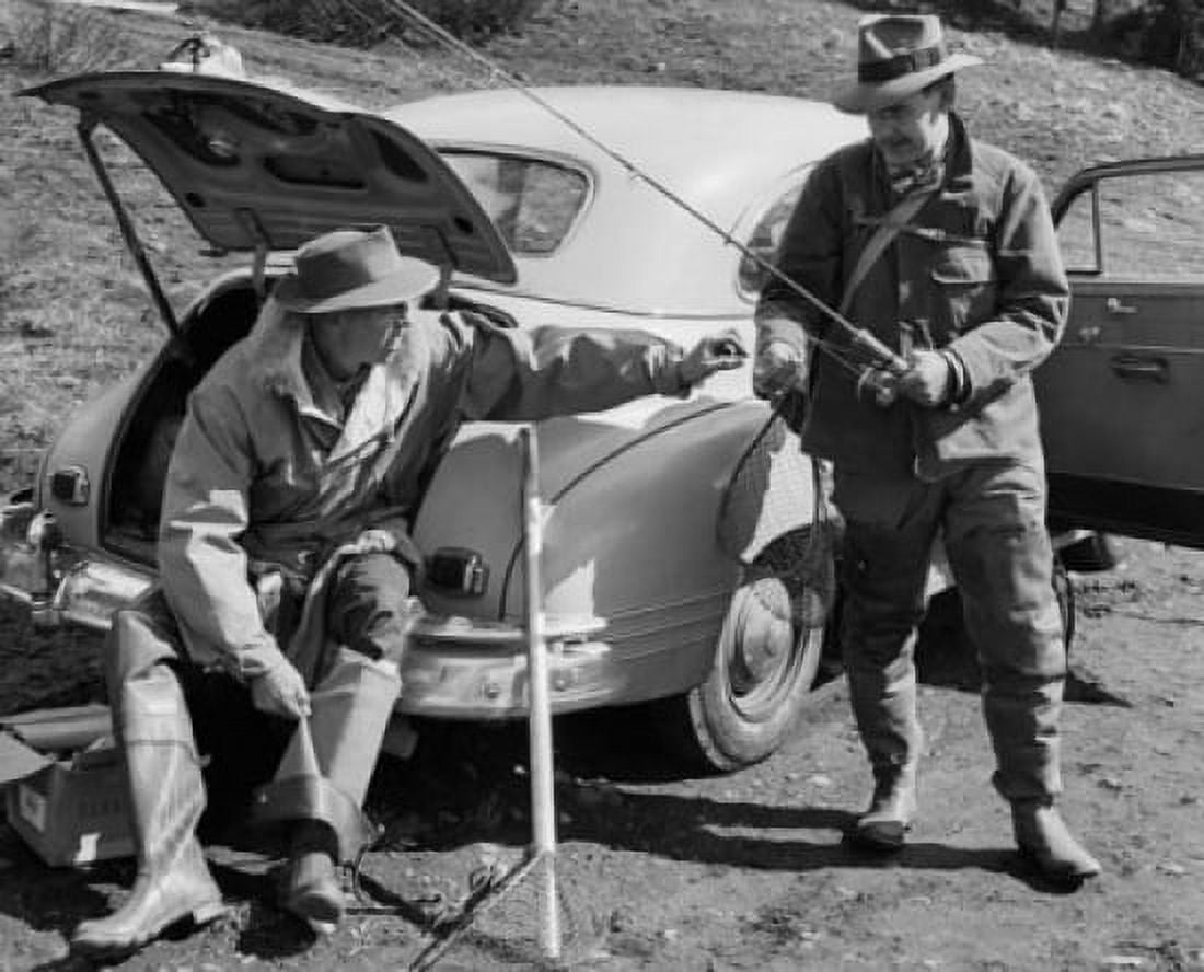 Mid adult man sitting in car trunk with another man standing beside him holding fishing rod Canvas Art -  (18 x 24)