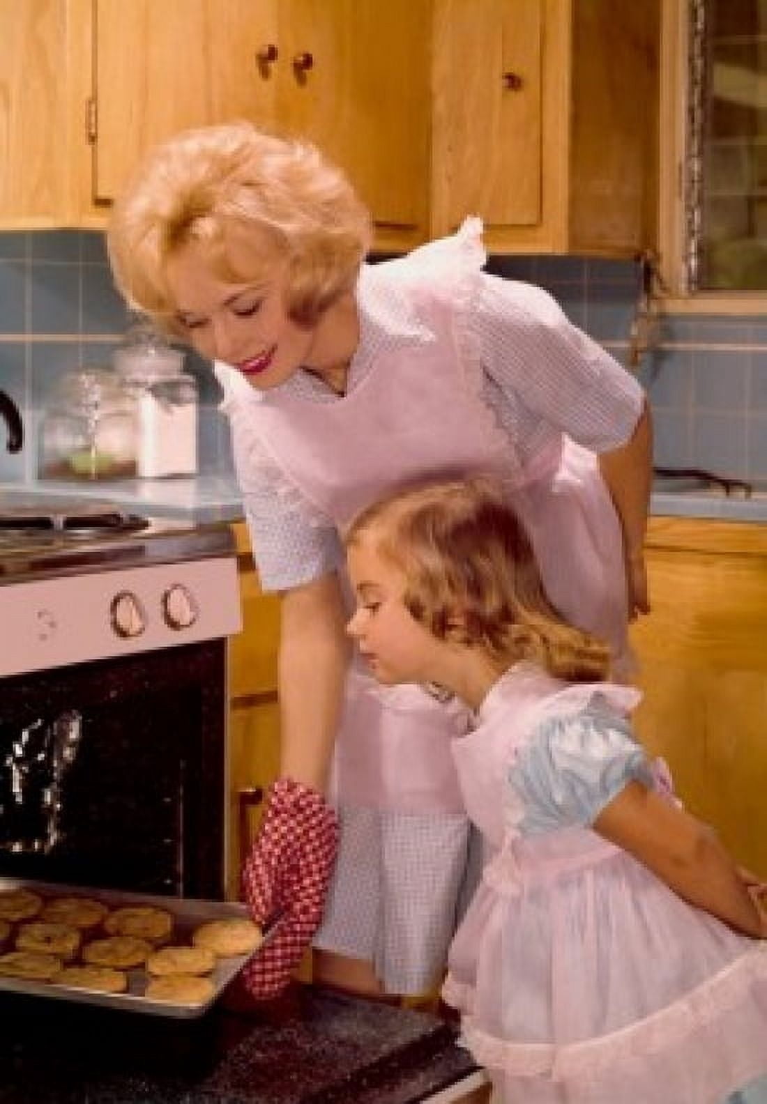 Mid adult woman putting cookies in an oven with her daughter standing beside her Canvas Art -  (24 x 36)