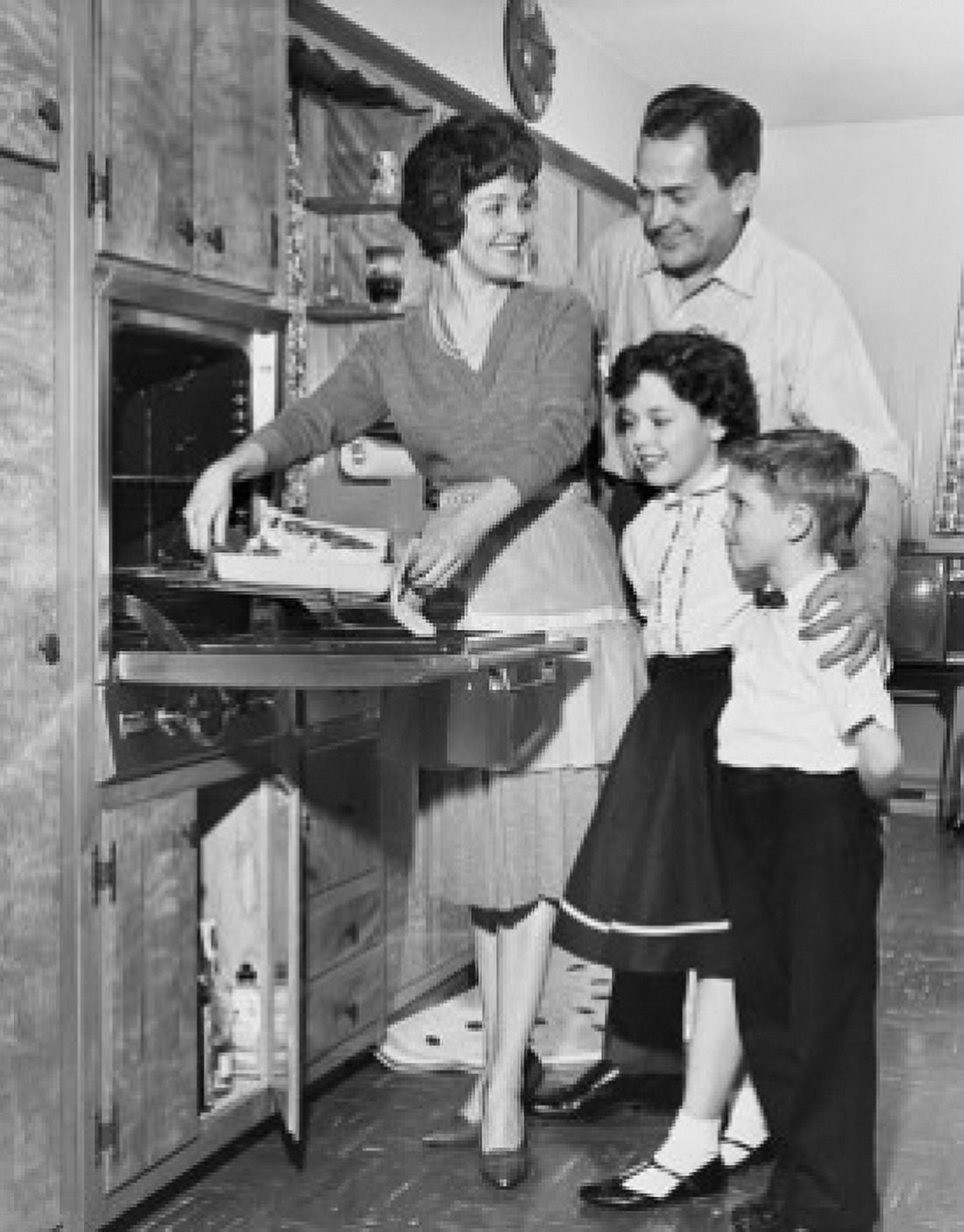 Mid adult woman putting food into an oven with a mid adult man and their children standing beside her Canvas Art - (24 x 36)