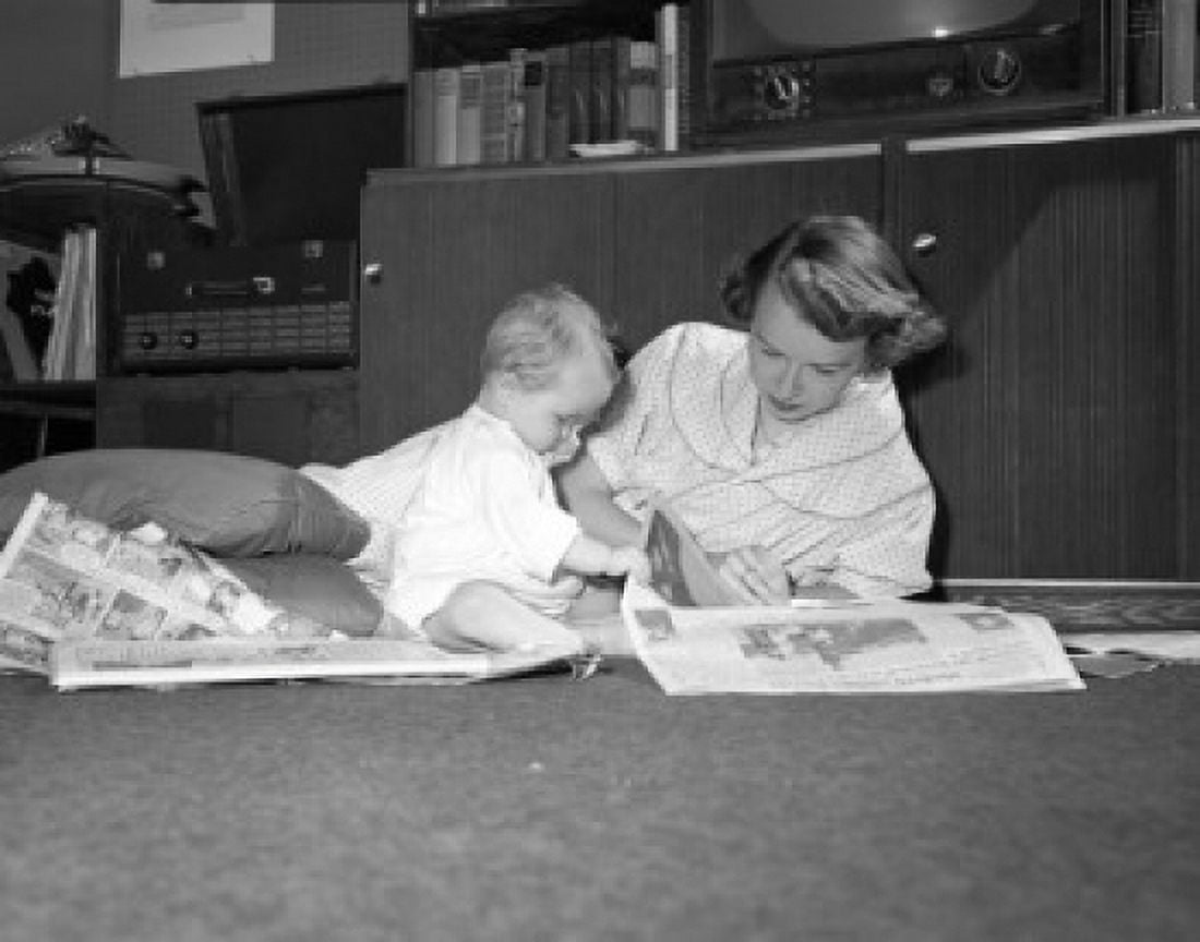 Mother and baby reading newspapers on floor Canvas Art - (18 x 24)