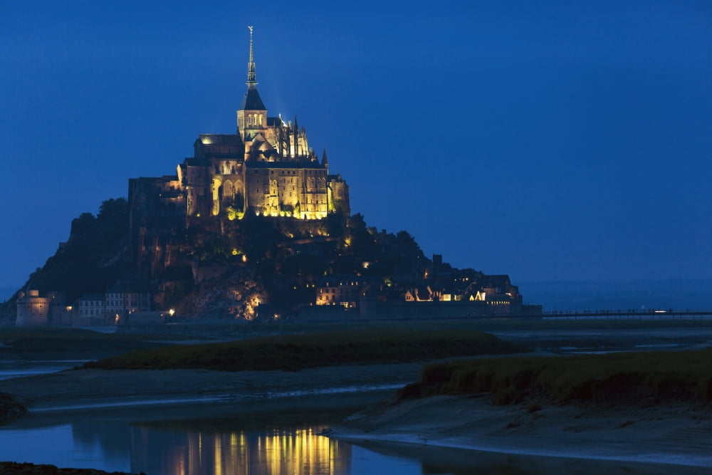 Night image of large stone Abbey perched on rocky island at low tide lit with flood lights with reflection in water Mont St Michel Brittany France Canvas Art - Michael Interisano Design Pics (19 x 12