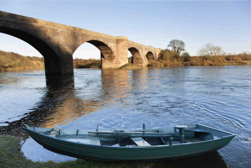 Northumberland England A Boat Moored On The Edge Of A River With A Bridge Canvas Art - John Short  Design Pics (38 x 24)