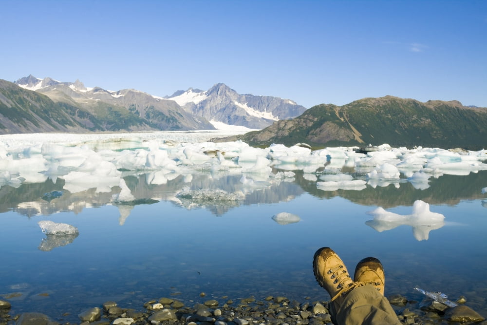 Person Relaxing Along Bear Glacier Lake With Feet Outstretched & Kenai Mountains In The Background Kenai Peninsula Southcentral Alaska Canvas Art - Michael DeYoung Design Pics (34 x 22)