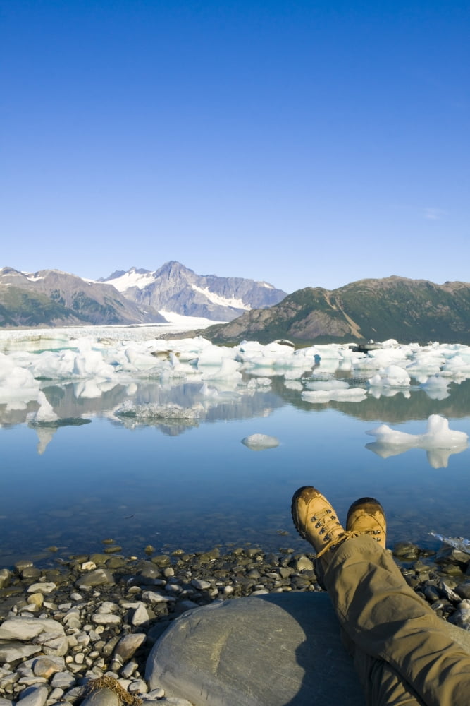 Person Relaxing Along Bear Glacier Lake With Feet Outstretched & Kenai Mountains In The Background Kenai Peninsula Southcentral Alaska Canvas Art - Michael DeYoung Design Pics (11 x 17)