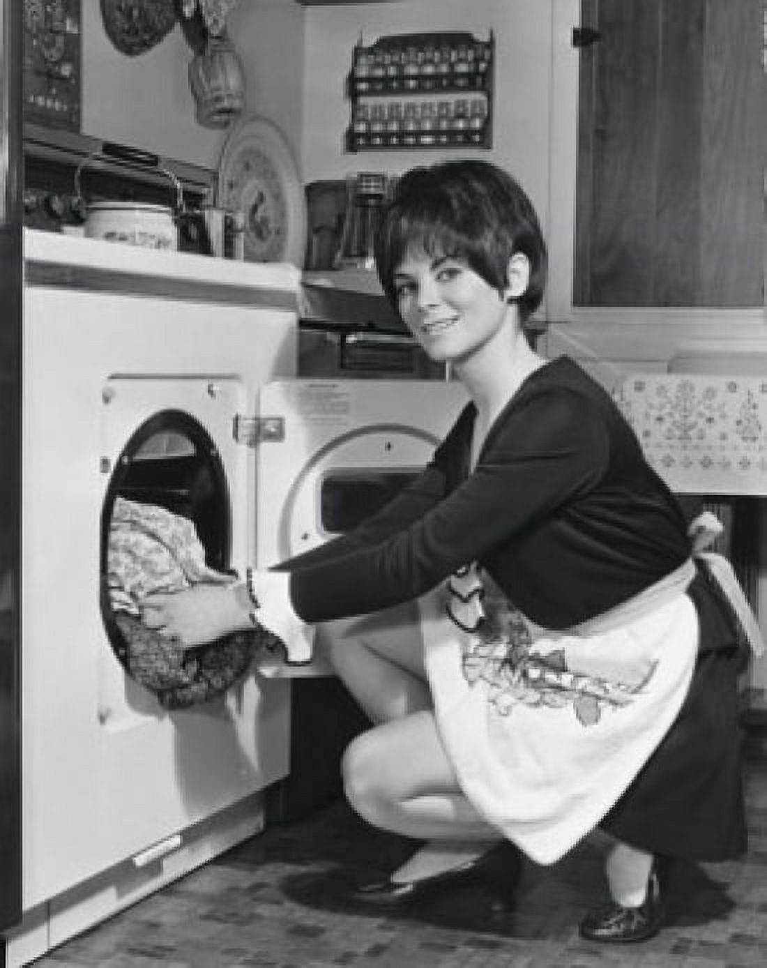 Portrait of a young woman putting clothes into a dryer Poster Print (24 x 36)
