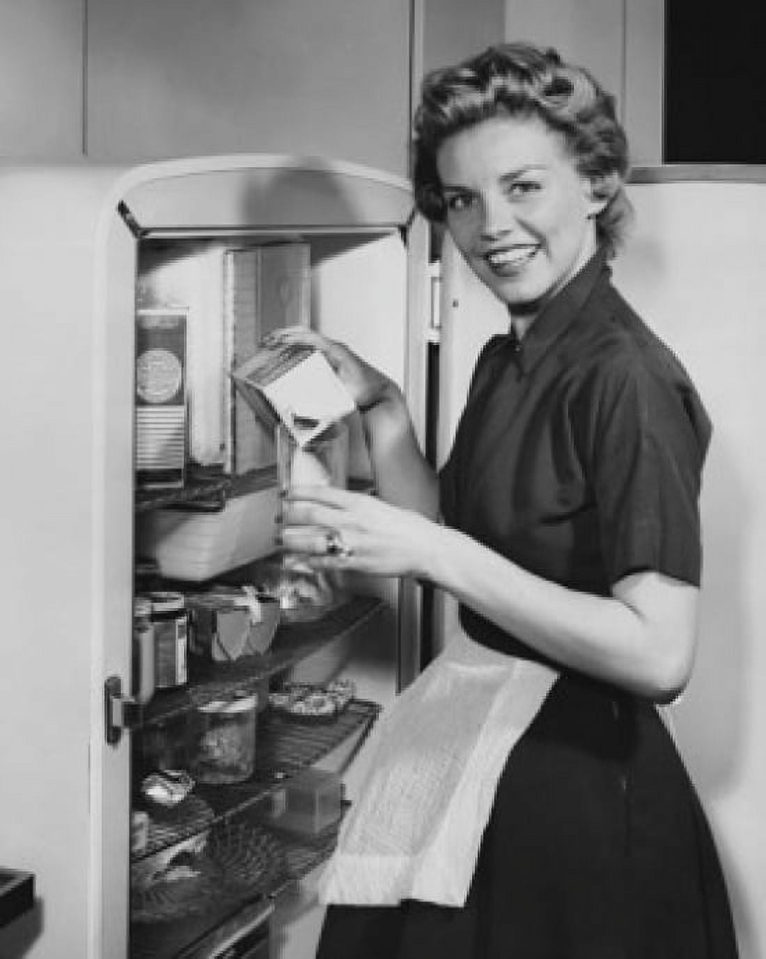 Portrait of a young woman standing in front of a refrigerator pouring milk into a glass Canvas Art - (24 x 36)