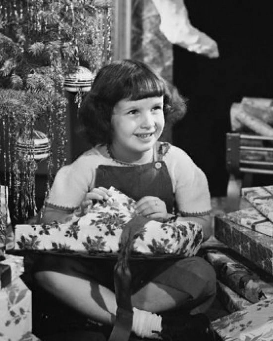 Posterazzi Girl sitting near a Christmas tree and opening a Christmas present Canvas Art - (24 x 36)