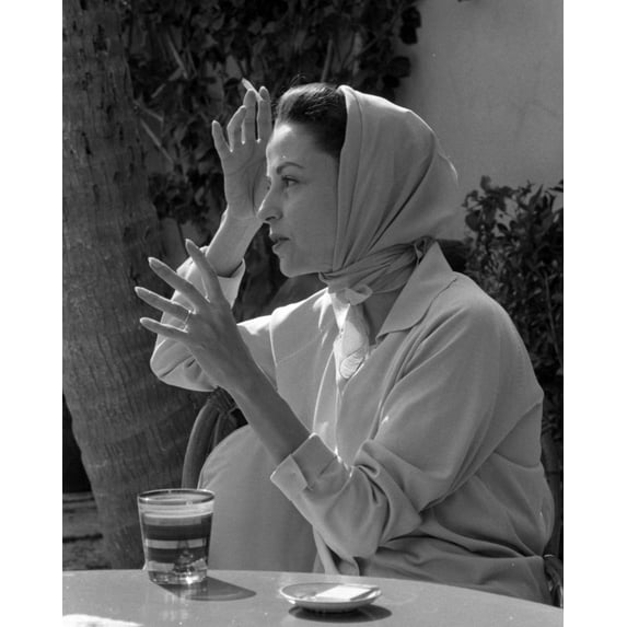 Print: Woman Wearing Headscarf Seated At Table With Drink, circa 1940
