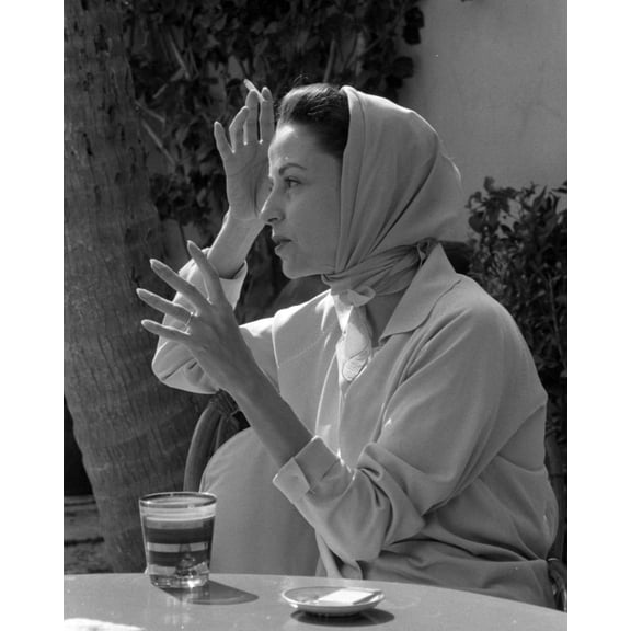 Print: Woman Wearing Headscarf Seated At Table With Drink, circa 1940