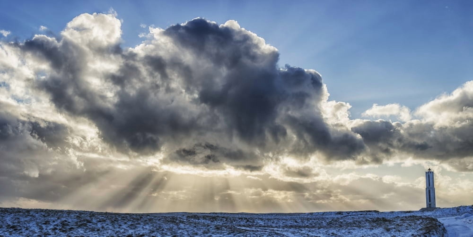 Rays of light shine out from behind the clouds in the skies above a lightnouse along the southern shore of Iceland Iceland Canvas Art - Robert Postma Design Pics (42 x 22)