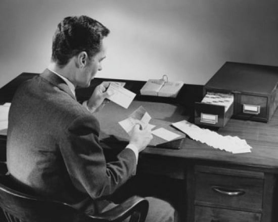Rear view of a businessman reading an index card and sitting at a desk in an office Canvas Art - (18 x 24)
