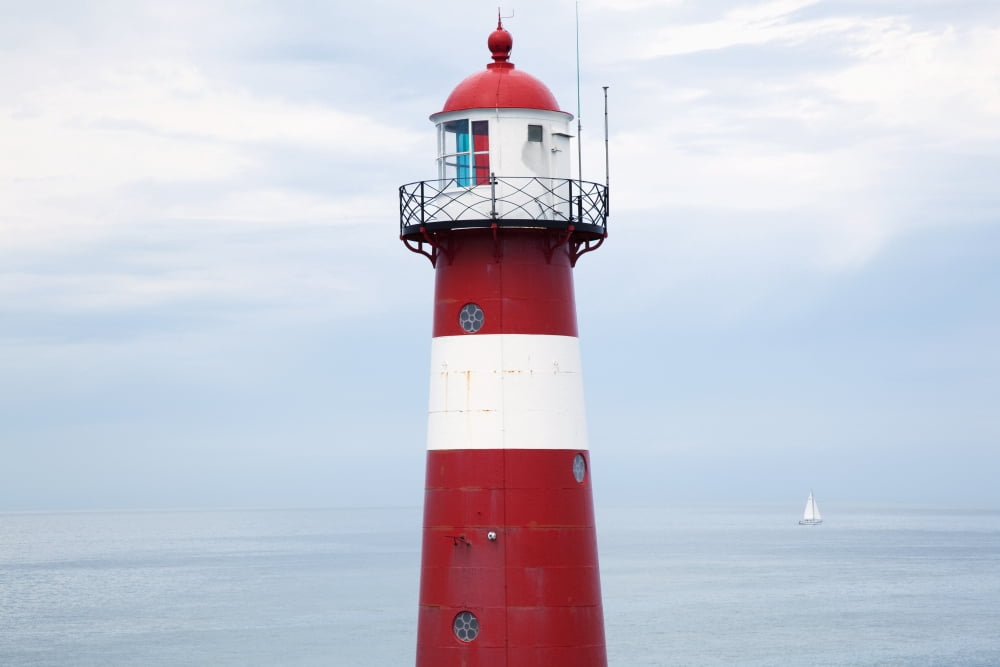 Red and white lighthouse along the coast with a sailboat in the distance near westkapelleZealand netherlands Canvas Art - Peter Zoeller Design Pics (19 x 12)