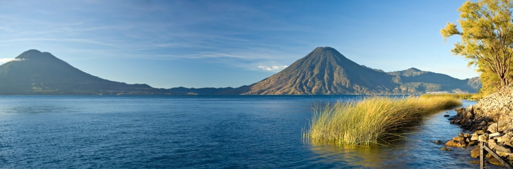 Reeds in a lake with a mountain range in the background Lake Atitlan Santa Cruz La Laguna Western Highlands Guatemala Canvas Art - Panoramic Images (27 x 9)