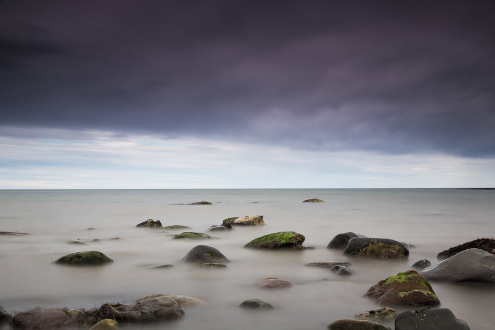Rocks in tranquil water under storm cloudsNorthumberland england Canvas Art - John Short Design Pics (38 x 24)