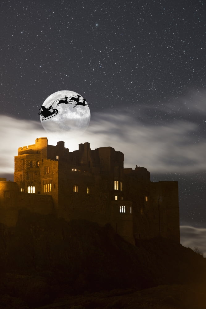 Santa in his sleigh and reindeer silhouetted in the starry sky in front of the moon over buildings Bamburgh Northumberland England Canvas Art - John Short Design Pics (12 x 19)