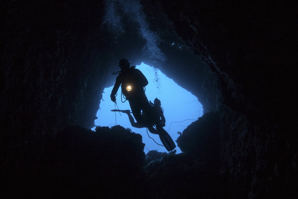 Scuba divers explore a cave near the island of Sulawesi Indonesia Canvas Art - Ethan DanielsStocktrek Images (34 x 23)