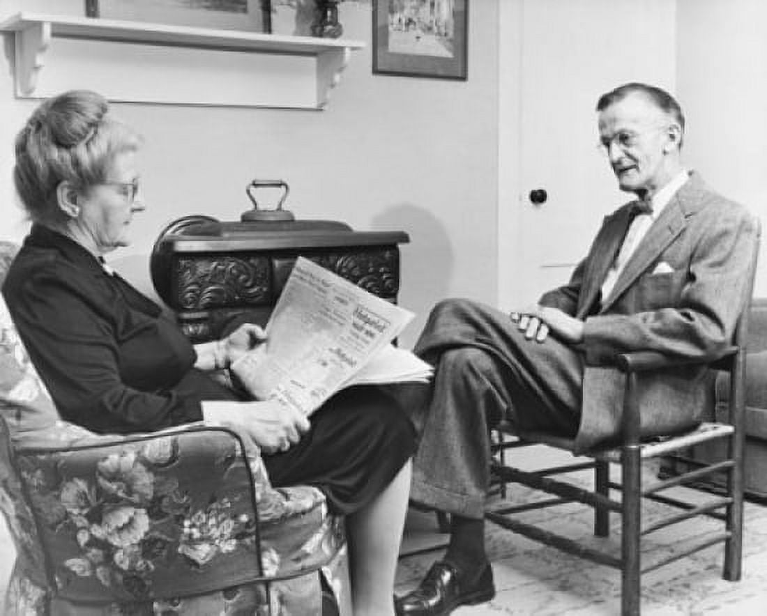 Senior woman reading a newspaper with a senior man sitting in front of her Canvas Art - (18 x 24)