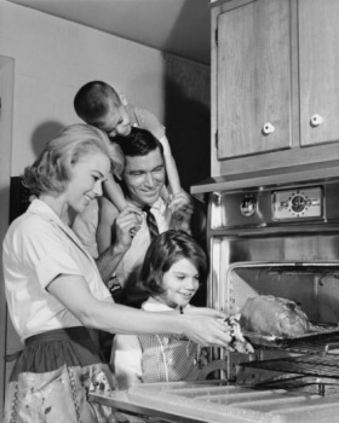 Side profile of a mid adult woman putting a turkey into an oven with her family standing beside her Canvas Art - (18 x 24)
