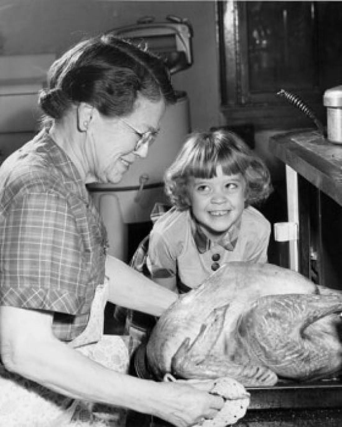 Side profile of senior woman putting roasted turkey in oven with her granddaughter smiling Canvas Art - (24 x 36)