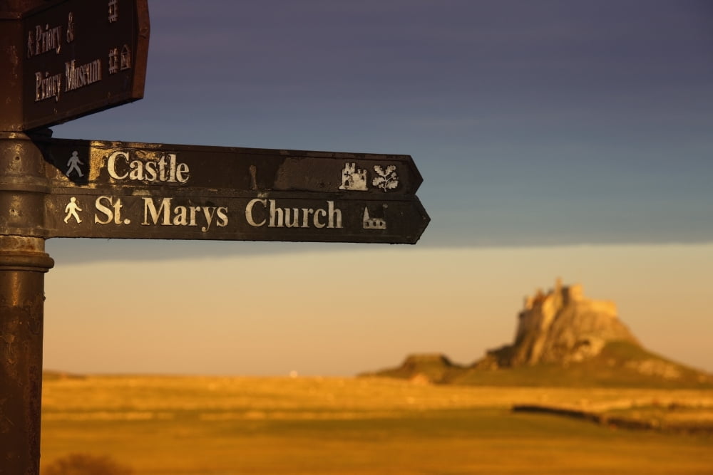 A Sign Post Pointing To A Castle And St Marys Church On The Tidal Island Also Known As Holy Island Lindisfarne Northumberland England Canvas Art - John Short Design Pics (19 x 12)