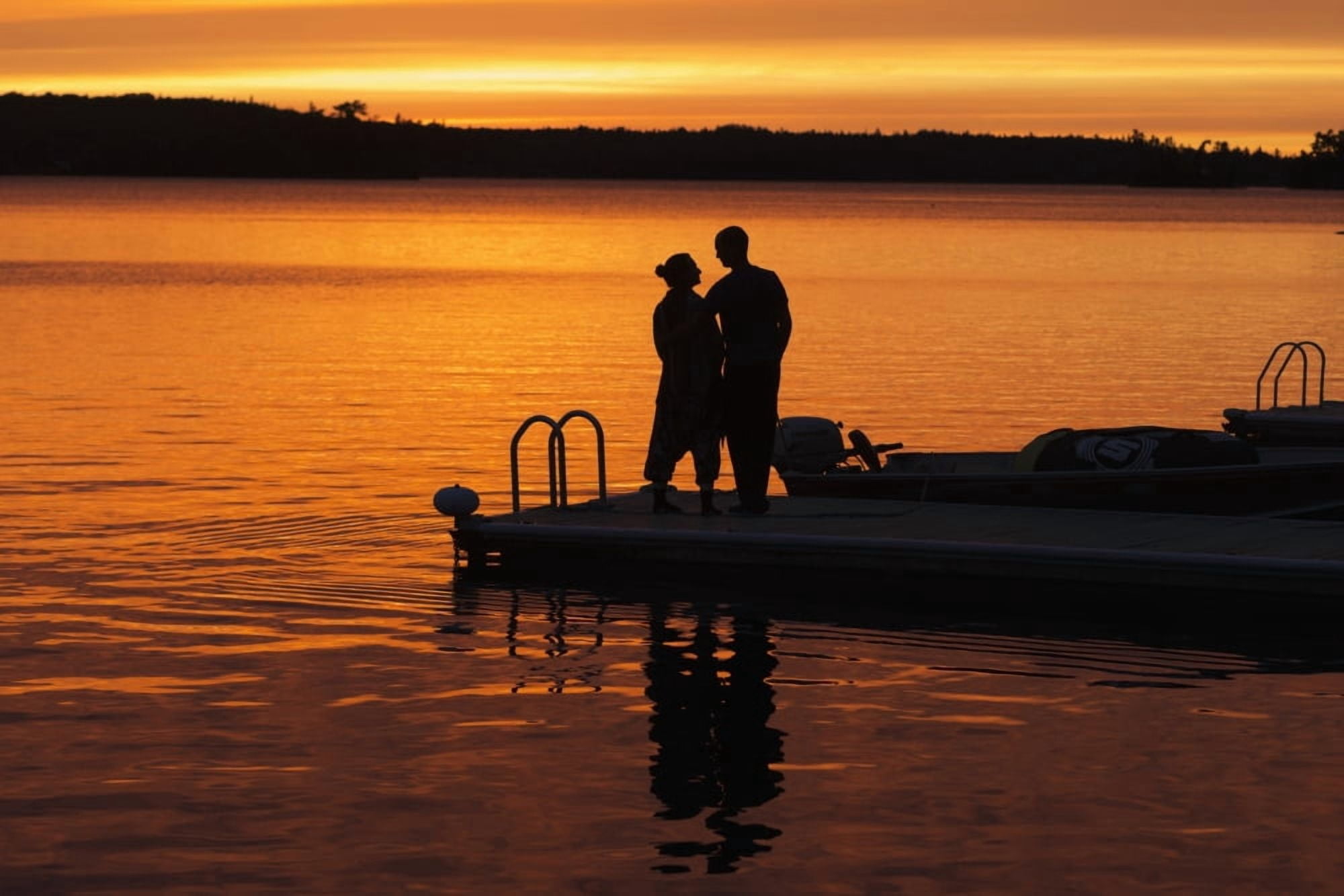 Silhouette of a couple standing at the end of a dock at sunset with an orange glow in the sky and reflected in the tranquil lake water Ontario Canada Canvas Art - Keith Levit Design Pics (38 x 24)